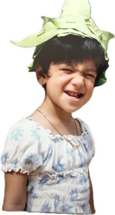 Usha as a toddler, grinning with her eyes scrunched shut, wearing a crown made of leaves